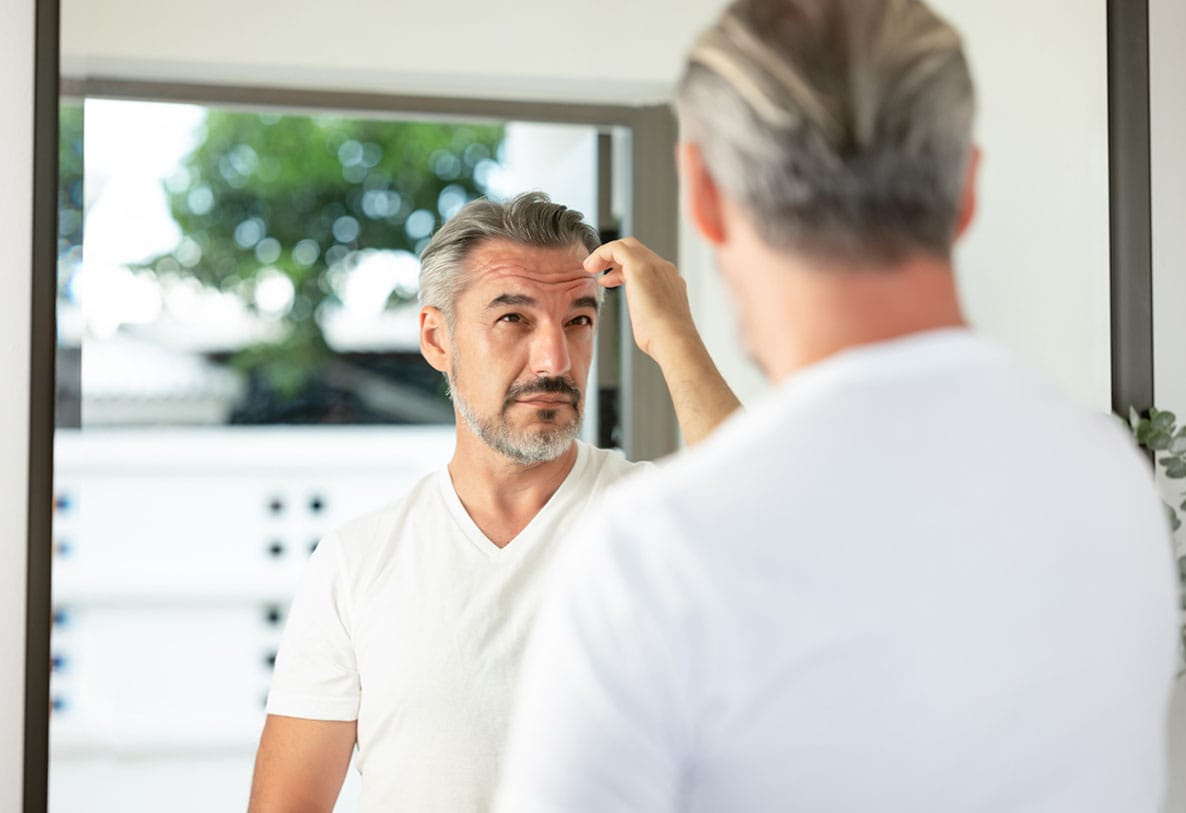 older man looking in the mirror after his artas robotic hair transplant in Miami, FL